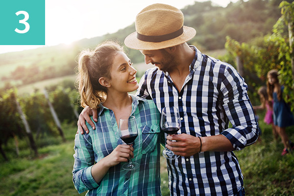 "Smiling couple in the countryside looking lovingly at each other whilst holding red wine glasses".